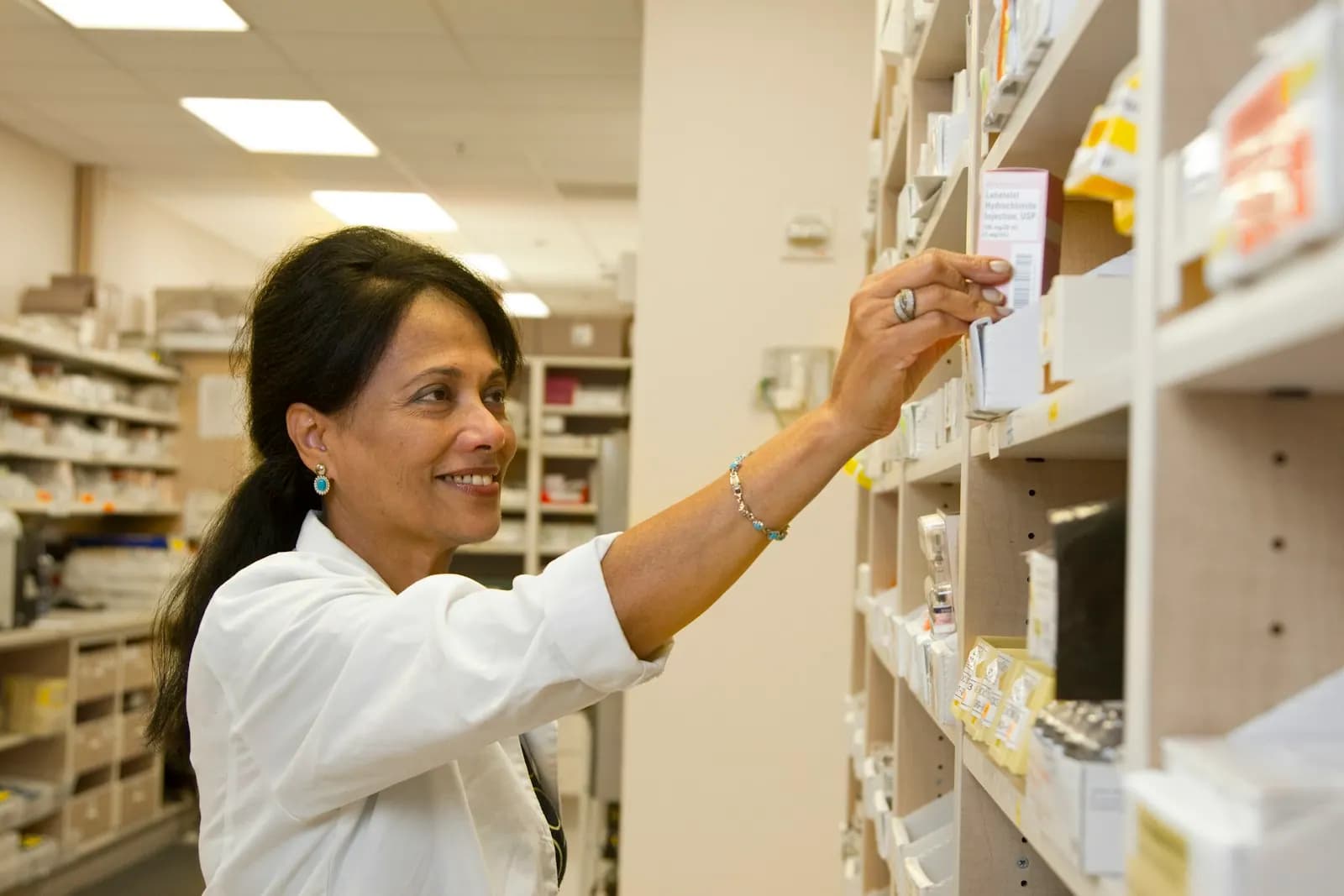 A pharmacist reaching for a carton on a pharmacy shelf